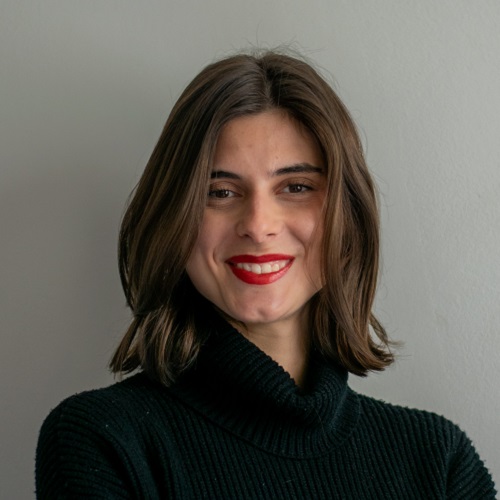 Claudia Negri's portrait, using a black turtleneck. Brown hairshoulder length hair, smiling with red lips.